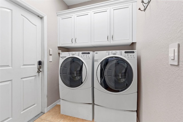 laundry room with washing machine and clothes dryer, light tile patterned floors, cabinet space, a textured wall, and baseboards