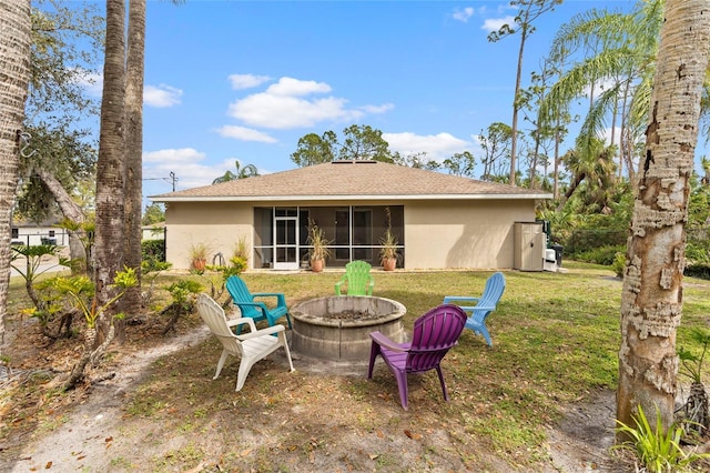 back of property with an outdoor fire pit, a sunroom, a yard, and stucco siding