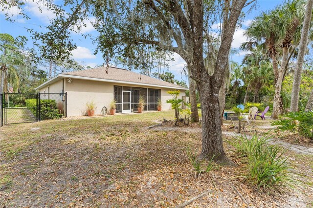 rear view of property with stucco siding, a gate, a sunroom, and fence