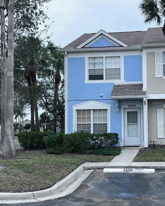 townhome / multi-family property featuring a shingled roof, uncovered parking, and stucco siding