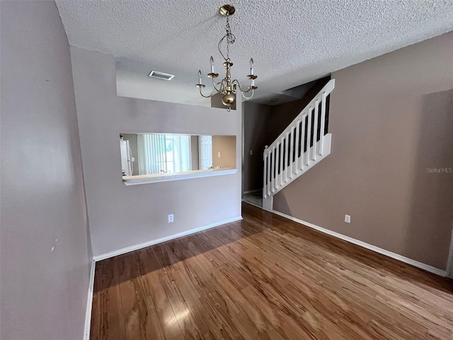 spare room with a notable chandelier, visible vents, stairway, wood finished floors, and baseboards