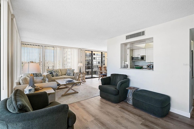 living room with visible vents, a textured ceiling, wood finished floors, a wall of windows, and baseboards