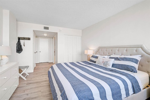 bedroom with light wood-style floors, a textured ceiling, visible vents, and a closet