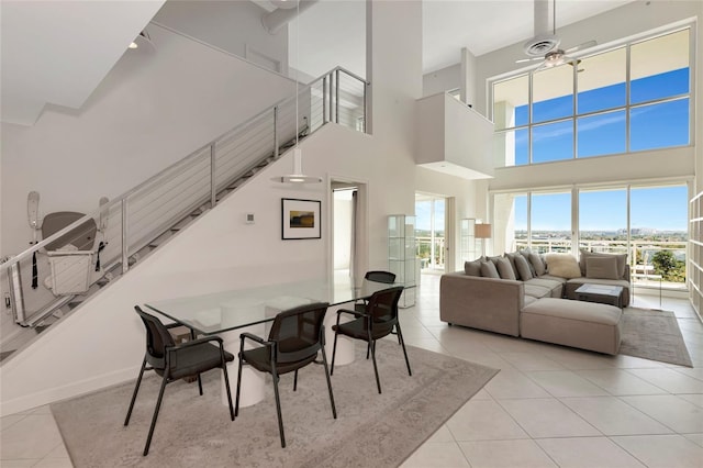 dining room featuring baseboards, a ceiling fan, stairway, a high ceiling, and light tile patterned flooring