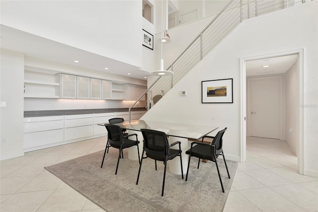 dining space featuring light tile patterned floors, recessed lighting, a high ceiling, baseboards, and stairs