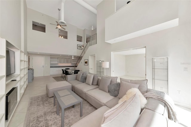 living room with a ceiling fan, light tile patterned flooring, a towering ceiling, and stairs