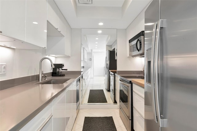 kitchen with light tile patterned floors, white cabinets, stainless steel appliances, a sink, and recessed lighting