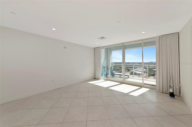 empty room featuring light tile patterned floors, recessed lighting, visible vents, baseboards, and a wall of windows