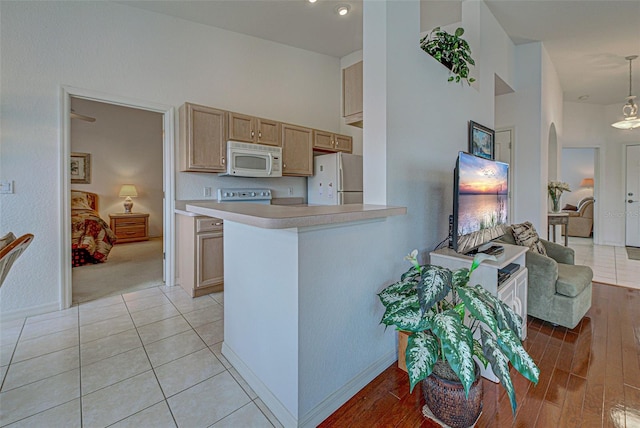 kitchen featuring arched walkways, a peninsula, white appliances, a high ceiling, and light countertops