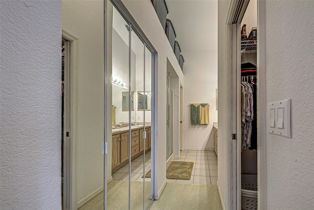 hall featuring light tile patterned floors, a textured wall, and baseboards