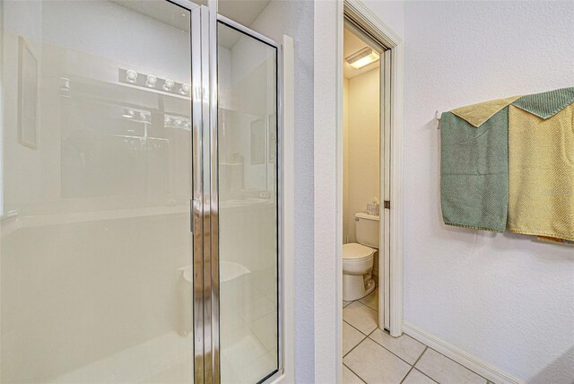 full bath with a textured wall, toilet, baseboards, a shower stall, and tile patterned floors