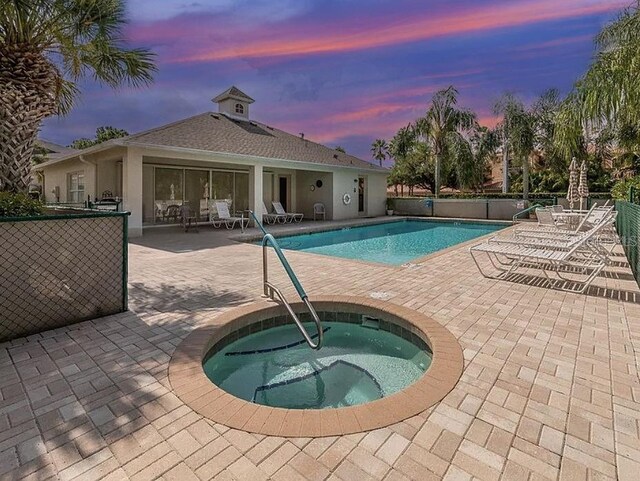 community pool with a patio, fence, and a hot tub