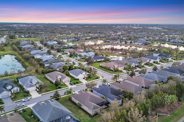 aerial view at dusk featuring a residential view and a water view