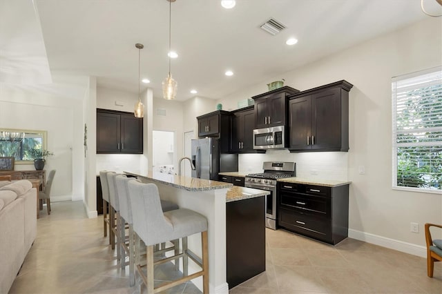 kitchen featuring stainless steel appliances, a breakfast bar, visible vents, backsplash, and light stone countertops