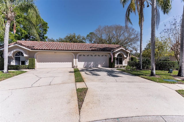 mediterranean / spanish-style home with an attached garage, driveway, a tiled roof, and stucco siding