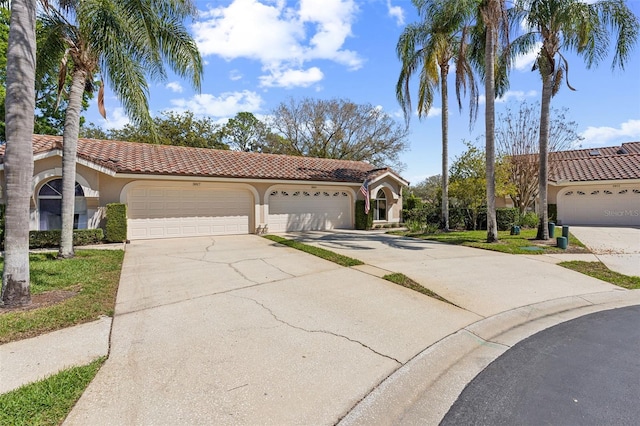 mediterranean / spanish house with an attached garage, driveway, a tiled roof, and stucco siding