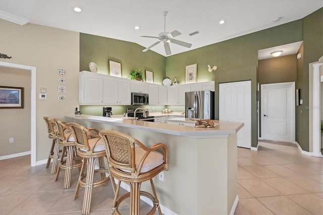 kitchen featuring light tile patterned floors, light countertops, appliances with stainless steel finishes, high vaulted ceiling, and a peninsula