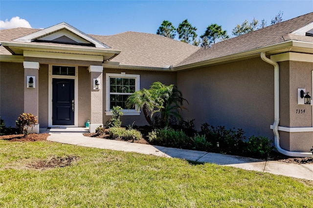 view of front facade featuring a shingled roof, a front yard, and stucco siding