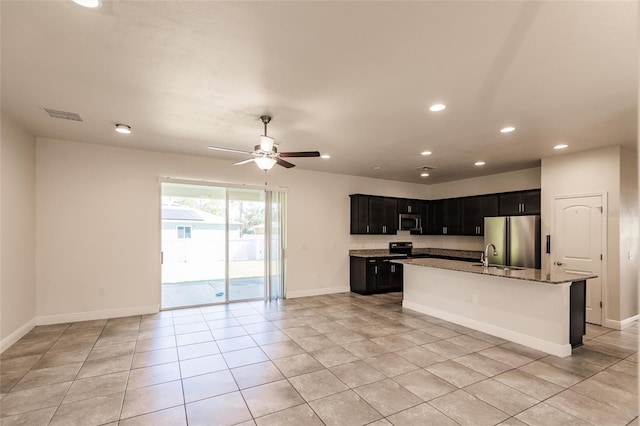 kitchen featuring visible vents, appliances with stainless steel finishes, open floor plan, dark cabinets, and light stone countertops