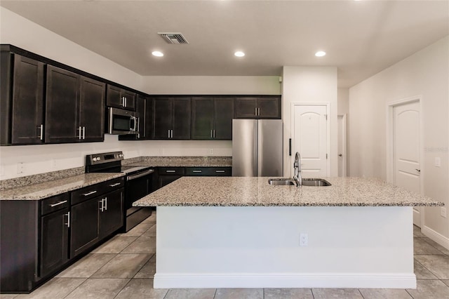 kitchen featuring visible vents, an island with sink, appliances with stainless steel finishes, light stone counters, and a sink