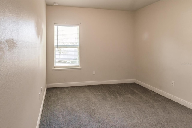 spare room featuring dark colored carpet and baseboards