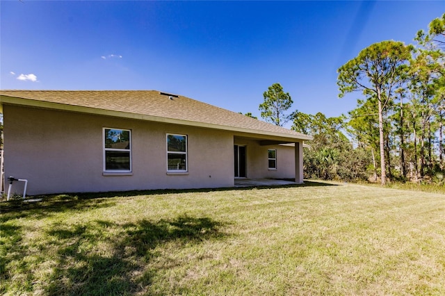 rear view of property with a shingled roof, a lawn, and stucco siding