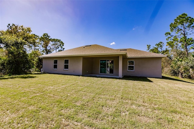 rear view of property featuring roof with shingles, a lawn, and stucco siding