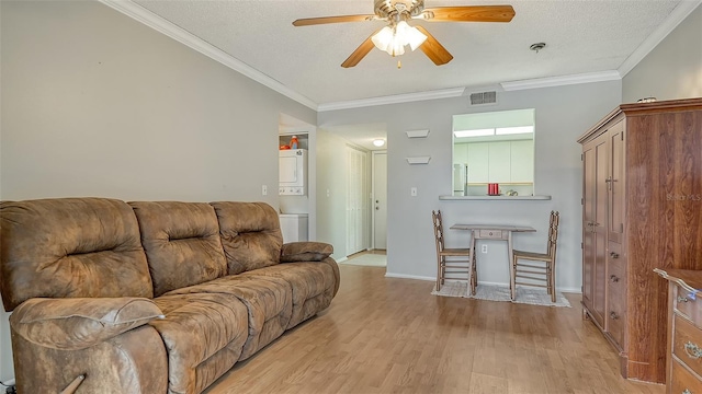 living room with stacked washer and dryer, crown molding, visible vents, and wood finished floors