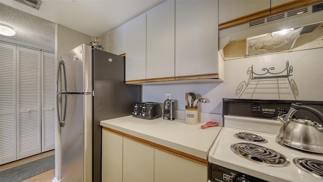 kitchen with under cabinet range hood, visible vents, light countertops, freestanding refrigerator, and white range with electric stovetop