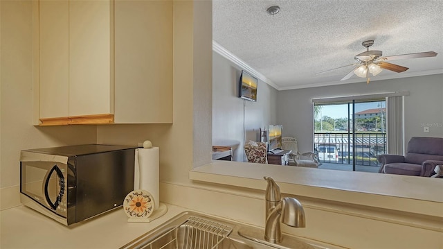 kitchen featuring a textured ceiling, open floor plan, light countertops, ornamental molding, and stainless steel microwave