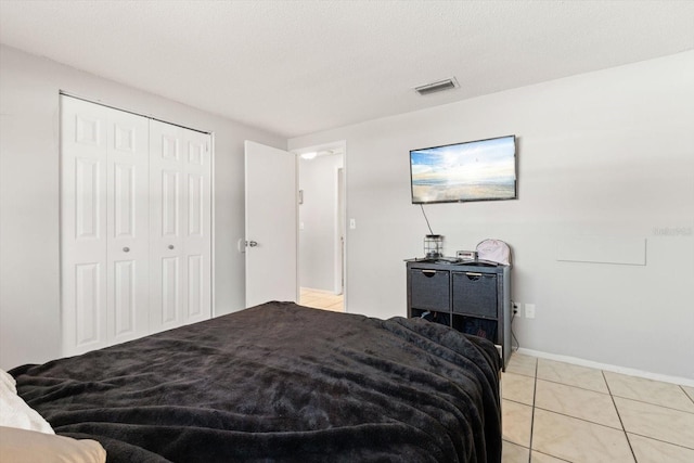 bedroom with light tile patterned floors, a textured ceiling, visible vents, baseboards, and a closet