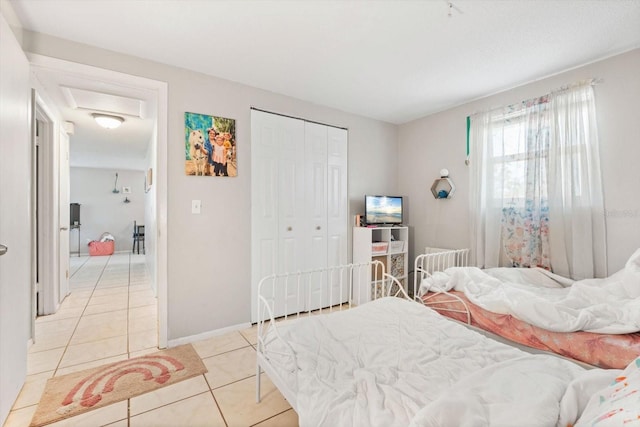 bedroom featuring light tile patterned floors, attic access, baseboards, and a closet