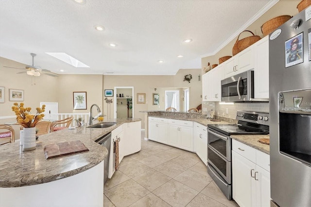 kitchen with a skylight, stainless steel appliances, tasteful backsplash, white cabinets, and a sink