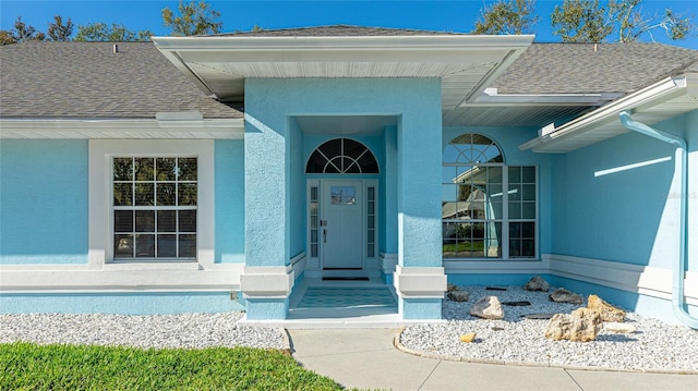 doorway to property with a shingled roof and stucco siding