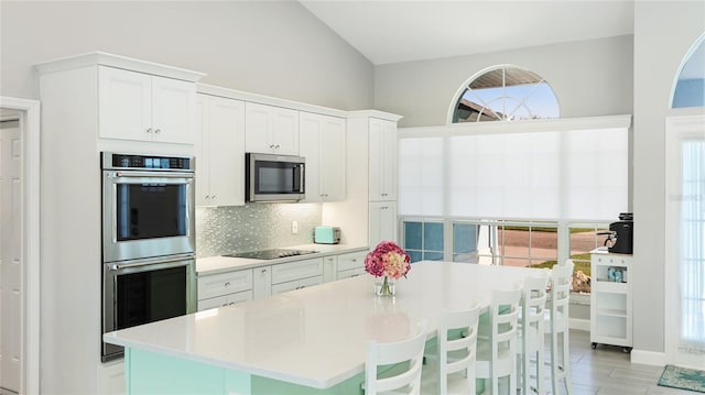 kitchen featuring decorative backsplash, a kitchen island, stainless steel appliances, light countertops, and white cabinetry