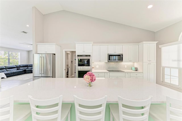 kitchen featuring tasteful backsplash, white cabinets, light stone counters, open floor plan, and stainless steel appliances