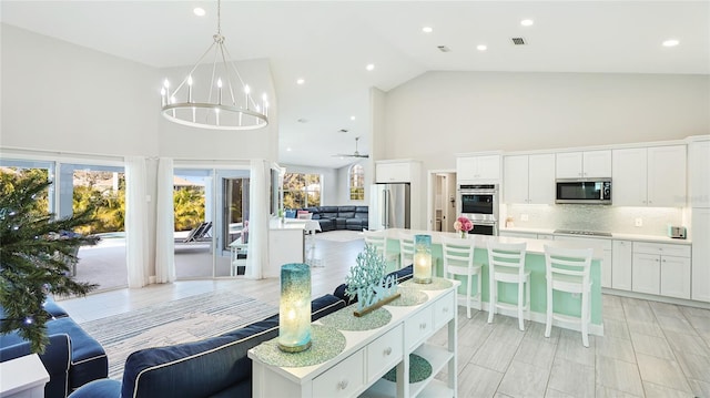 interior space with open floor plan, high vaulted ceiling, stainless steel appliances, white cabinetry, and backsplash