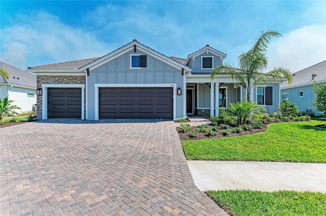 view of front of home featuring an attached garage, stone siding, decorative driveway, a front lawn, and board and batten siding