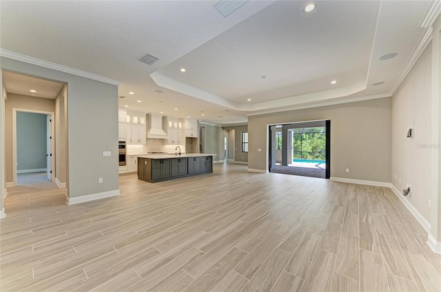 unfurnished living room featuring light wood-style flooring, visible vents, a raised ceiling, and a sink