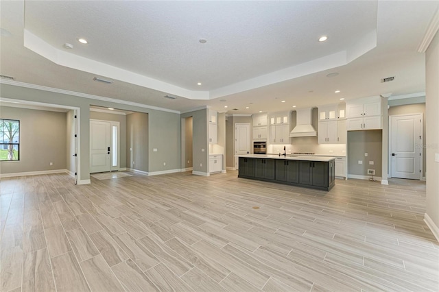 unfurnished living room with a tray ceiling, light wood finished floors, visible vents, a sink, and baseboards