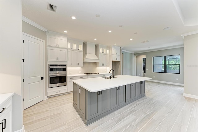 kitchen featuring wood tiled floor, crown molding, stainless steel double oven, premium range hood, and a sink