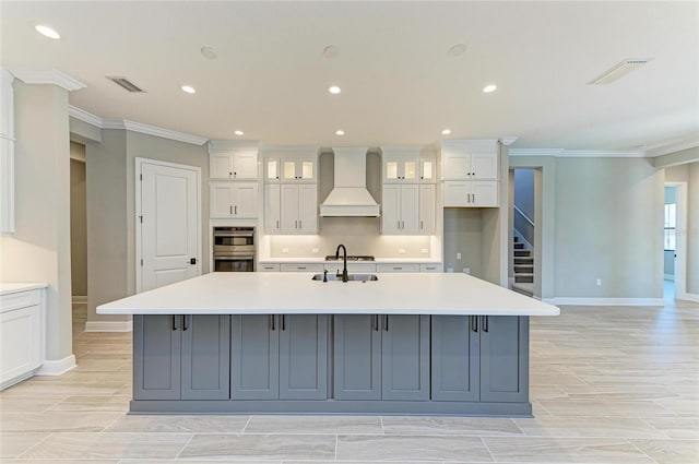 kitchen featuring light countertops, premium range hood, a sink, and a large island with sink