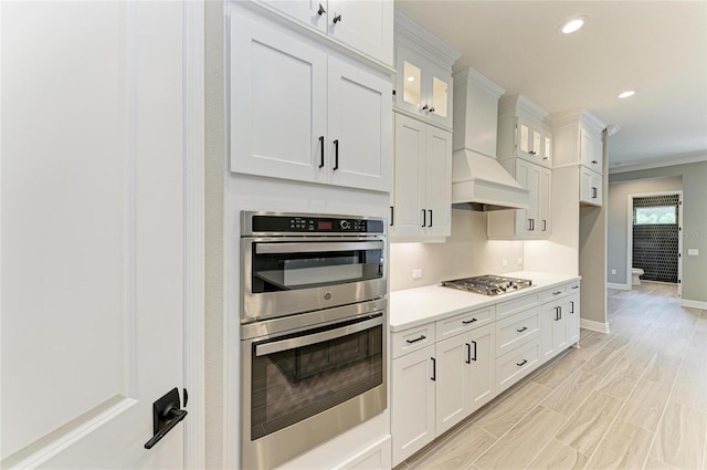 kitchen with white cabinets, glass insert cabinets, appliances with stainless steel finishes, light countertops, and premium range hood