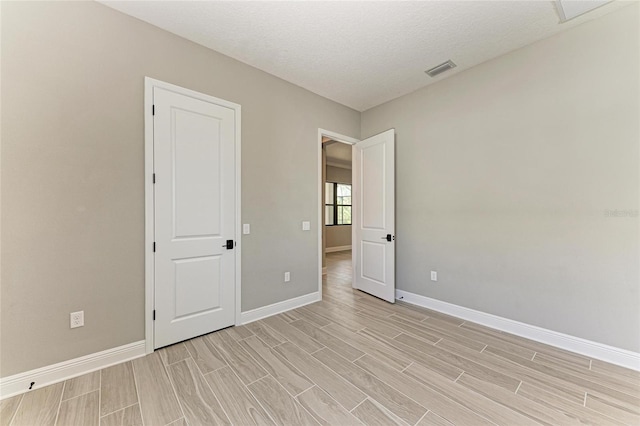 unfurnished room featuring wood finish floors, visible vents, a textured ceiling, and baseboards