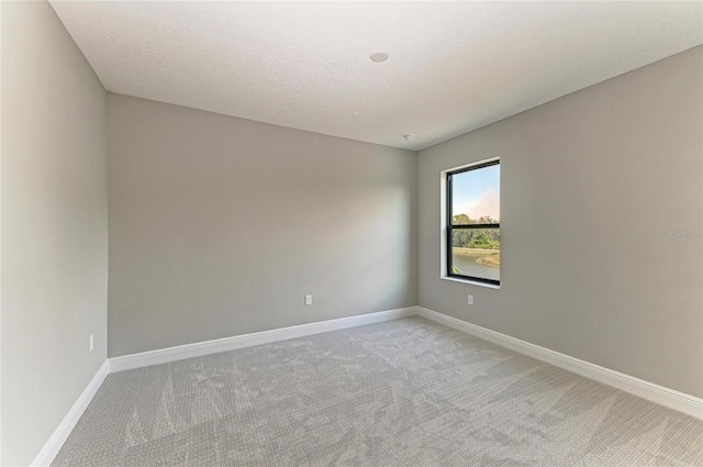 spare room featuring a textured ceiling, light colored carpet, and baseboards