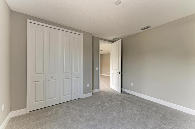 unfurnished bedroom featuring a textured ceiling, carpet flooring, visible vents, baseboards, and a closet