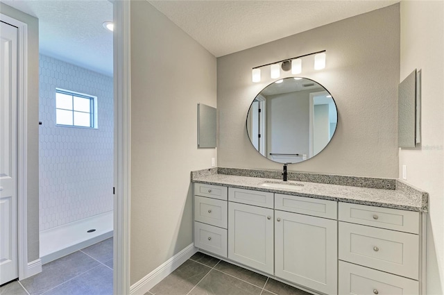 bathroom with tile patterned flooring, tiled shower, a textured ceiling, and vanity