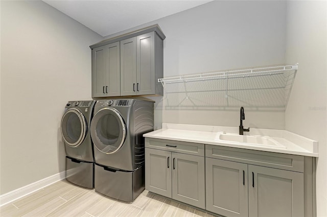 laundry area with cabinet space, washing machine and dryer, wood tiled floor, a sink, and baseboards