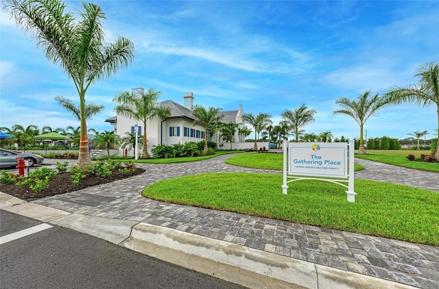 community sign featuring decorative driveway and a lawn