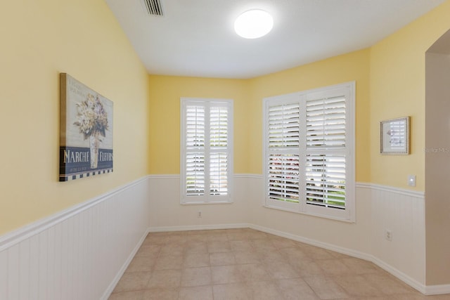 empty room with arched walkways, a wainscoted wall, and visible vents